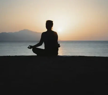 Silhouette di una persona in meditazione sulla spiaggia al tramonto, simbolo di tutti gli stili di yoga.